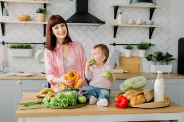 mother and kid daughter cooking in the kitchen . Mom holds pepper in her hand and her daughter holds the apples and eats them