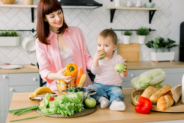 Mother with her daughter in the kitchen preparing healthy food with fresh vegetables, home parenting life style