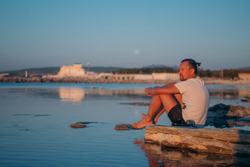 Fototapeta na wymiar A young man sits on a stone by the sea.