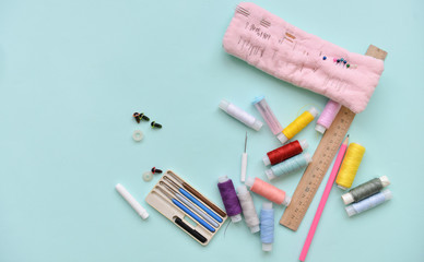 sewing accessories for needlework threads of different colors ruler, crochet hooks and needles lie on an isolated blue background.