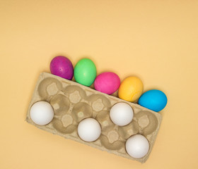 Pure unpainted white eggs and Colorful Easter eggs in tray isolated on beige. Nine eggs. 