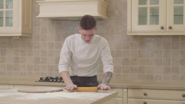 Rolling dough with rolling pin for pizza preparation on table. Chef rolling dough for pie with wooden roller. Baking bread and cake in bakery. Chef cook cooking food on kitchen table