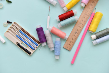 sewing accessories for needlework threads of different colors ruler, crochet hooks and needles lie on an isolated blue background.