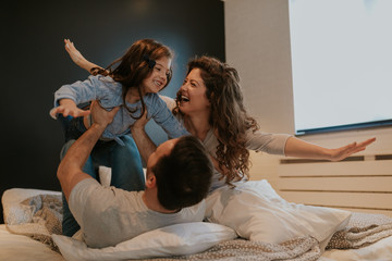 Family spending free time at home. Cheerful family having fun with their daughter on the bed.