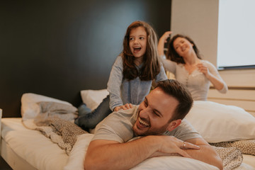 Parents having fun with their little daughter on bed. Family spending time at the morning.