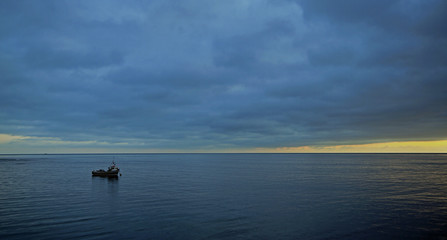 A lone boat is moored on a flat sea at sunrise