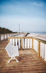Naklejka premium Empty bench on a wooden boardwalk by a beach