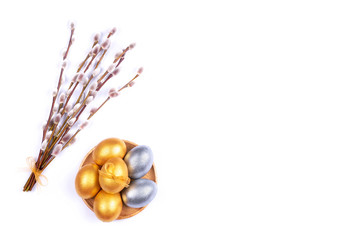 Golden and silver colored Easter eggs on wooden plate with willow catkins branches isolated on white background. Place for text.