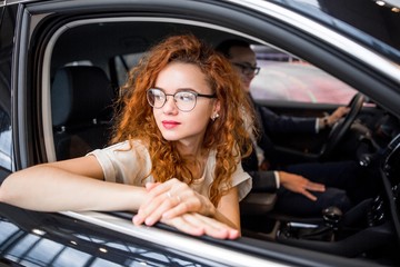 Young independent business lady with glasses sitting on the passenger seat in a car with a driver