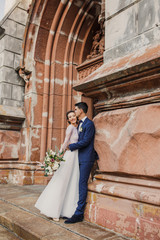 Fototapeta na wymiar young beautiful couple bride and groom walk in the city on the background of the church and smile the bride in a beautiful dress the groom dressed stylishly