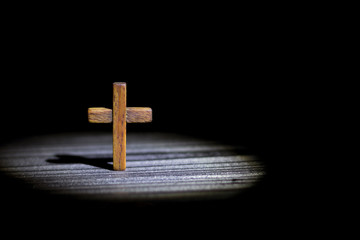 the cross stands on a dark wooden background in a ray of light in the dark