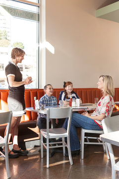 Friendly, smiling waitress server in uniform taking order from family dining in casual restaurant