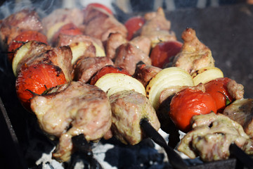 Juicy shish kebab from pork and tomatoes, fried on a fire outdoor.