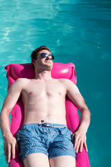 Man in his 20s on vacation relaxing in an outdoor swimming pool in the sun. Guy in a swimming pool on a raft. Enjoying the summer, carefree. Escaping reality.