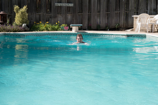 Young man doing breast stroke in an outdoor swimming pool on a sunny day. Fit white man swimming laps in an outdoor swimming pool in the summer. Diving board in the background. Exercising in pool.