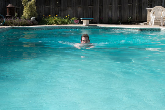 Young man doing breast stroke in an outdoor swimming pool on a sunny day. Fit white man swimming laps in an outdoor swimming pool in the summer. Diving board in the background.
