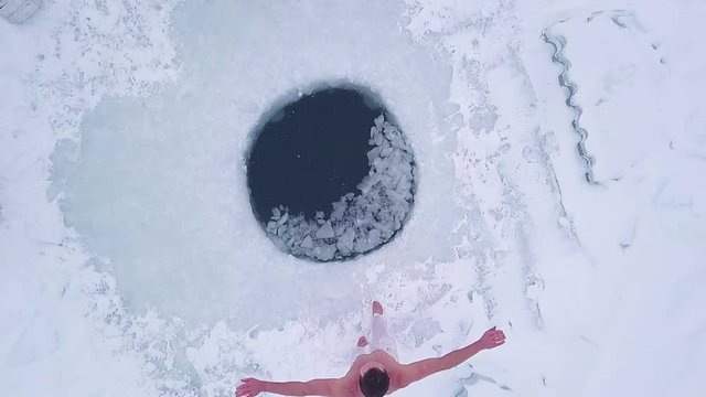 Man jumps into the ice hole. Aerial top down view