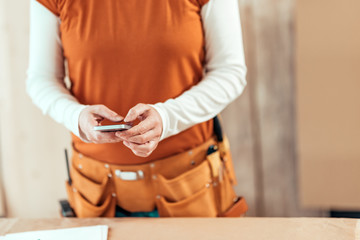 Female carpenter is using mobile phone for text messaging