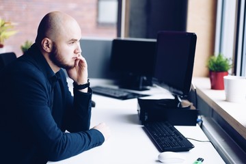Thoughtful man working in office on laptop computer