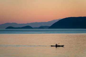 Kayaking at Sunset Through the San Juan Islands of Washington State. A kayaker paddles past Orcas Island in the Salish Sea during a beautiful sunset.