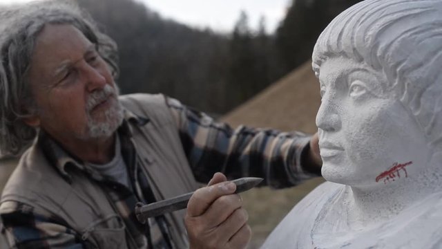 Senior sculpting in a stone with chisel