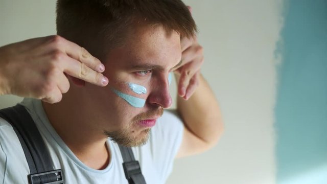 Builder man paint on his face battle color to paint the walls in the apartment or house. Construction, repair and renovation.