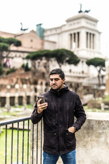 Young handsome man typing on the phone on Rome street with Forum on background