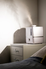 Aroma oil diffuser on the bedside table at night at home, steam from the air humidifier, vertical. Ultrasonic technology, increase in air humidity indoors. 