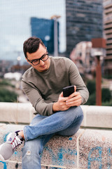 Man texting on phone. Casual man using smartphone smiling happy outside office building. Outdoor portrait of modern young guy with mobile in the street