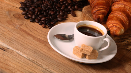 Coffee white cup, croissants on wooden table and roasted coffee beans. Breakfast concept