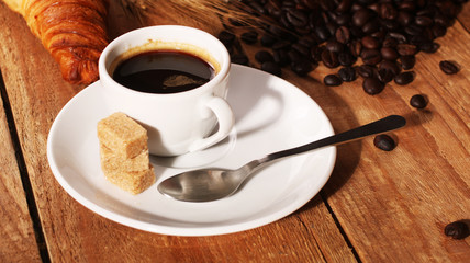 Coffee white cup, croissants on wooden table and roasted coffee beans. Breakfast concept