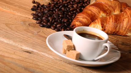 Coffee white cup, croissants on wooden table and roasted coffee beans. Breakfast concept