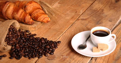 Coffee white cup, croissants on wooden table and roasted coffee beans. Breakfast concept