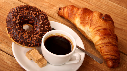 Coffee white cup, croissants on wooden table and roasted coffee beans. Breakfast concept