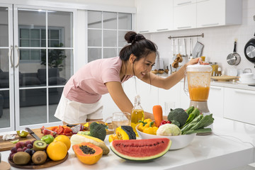 Beautiful young woman making fresh juice from vegetables and fruits in kitchen at home.