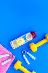 Fitness set with bars, towel, bottle of water and wrist builder on blue background top view mock up