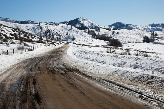Rugged dirt road in winter with snow and mountains