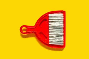 Red dustpan and brush lying on yellow background. In the style of pop art. Top view.