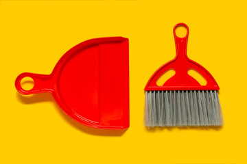 Red dustpan and brush lying on yellow background. In the style of pop art. Top view.