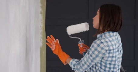 Young woman singing and painting interior wall of new apartment