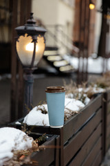 Mockup ad: a blank paper cup standing on a fence in an old town background