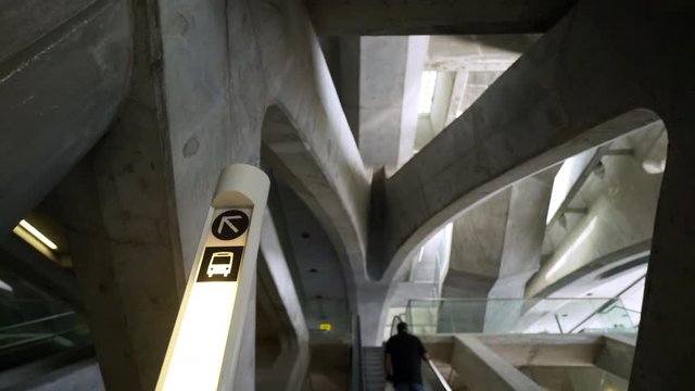 From below of sign post showing direction to bus stop under concrete ceiling. Concept of modern train station or airport terminal in big capital city