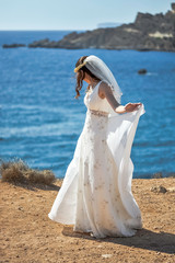 Fototapeta na wymiar Beautiful bride in a glamorous white wedding dress with scenic sea view on a cliff, Malta.
