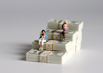Miniature women sitting with babies on a pile of banknotes stacked in the shape of a staircase.