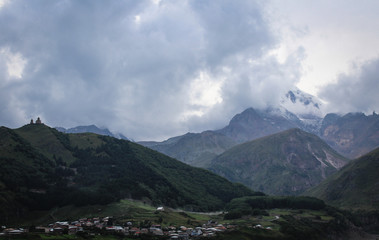 Fototapeta premium The main Caucasian ridge. Georgia, Kazbegi village (Stepantsminda). Mount Kazbek. Mountains, summer, twilight. Beautiful, amazing sky. High mountains. Vacation, hike. christian Gergeti Trinity Church