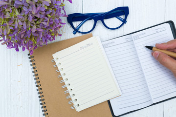 Man hand writing on blank page of notebook paper with pen, glasses and office supplies, top view.