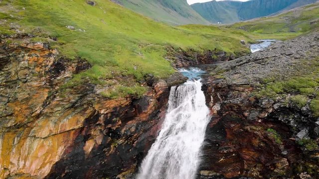 Long waterfall in norway seen from above and then moving to the ground until the drone has a zenital image of the water falling