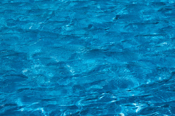 Blue and bright ripple water surface in swimming pool with sun reflection.