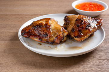 close up of grilled chicken thigh in a ceramic dish served with sweet chilii sauce on wooden table. homemade style food concept.