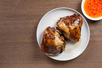 top view of grilled chicken thigh in a ceramic dish served with sweet chilii sauce on wooden table. homemade style food concept.